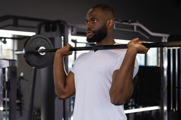 Fototapeta na wymiar Fit and muscular african man lifting heavy barbell weight at the gym.