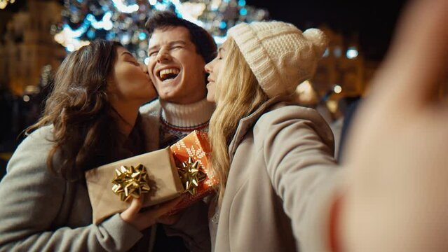 three friends with gifts at christmas night at old town square call their relatives via video link. Friendship, christmas, new year, holiday concept. New York