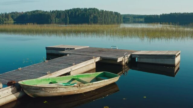 Drone flies over wooden old boat moored at the pier on a large lake among the forest and trees at dawn on a summer day