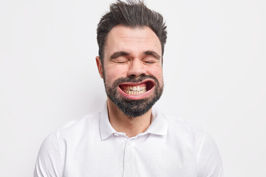 Close up portrait of handsome bearded dark haired man clenches teeth has widely opened mouth dressed in shirt isolated over white studio background. Human facial expressions and emotions concept