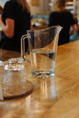 A decanter with drinking water on a wooden table. Interior of a cozy coffee shop. White paper napkins. Glass transparent decanter. Vertical photo.