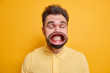 Portrait of dark haired man has widely opened mouth on strong wind shows white teeth dressed in...