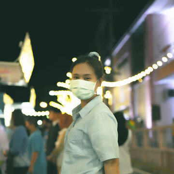 Asian women wearing masks Go to an event that is held at night. It is decorated with many light bulbs, creating a circular bokeh in the background.