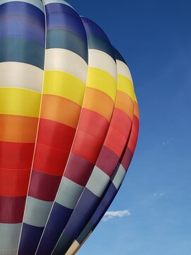 Vertical photo from directly below, looking up at the outside of a red, blue, yellow and white hot air balloon with a deep blue sky and copy space.