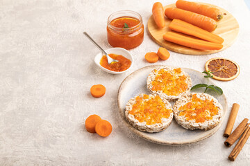 Carrot jam with puffed rice cakes on gray concrete. Side view, copy space.