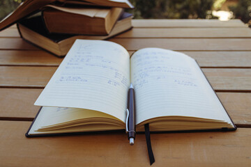 Open notebook with pen and pile of old books on garden table