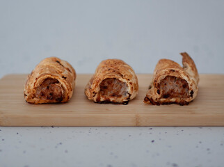 Three sausage rolls on a wooden serving board against a white speckled background.