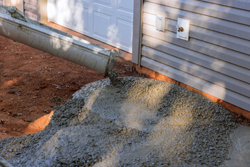 On site new home in process of construction, worker pours wet concrete as he paves driveway.
