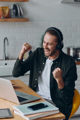 Excited young man in headphones gesturing while looking at laptop