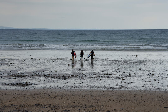 Paddleboarders walk to the sea at Oxwich Bay,