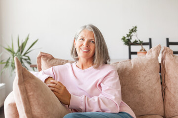 Portrait happy healthy middle aged woman sitting on comfortable couch at home - Powered by Adobe