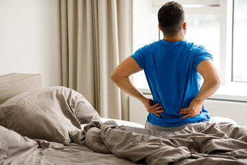 Rear view of a man touching and massaging his spine suffering from pain after sleeping on an...