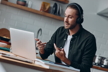 Handsome young man in headphones talking and gesturing while having web conference from home