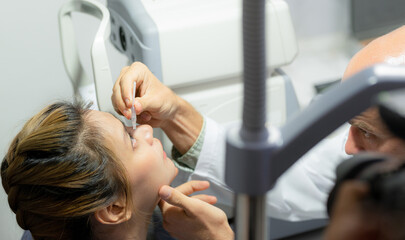 An ophthalmologist puts artificial tears in the girl's eyes.