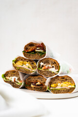 Photo of a delicious freshly made sandwiches from brown bread with meat, red fish, greens, sauce, eggs, cheese and other sandwich ingredients on a white modern porcelain plate on a white background  