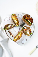 Photo of a delicious freshly made sandwiches from brown bread with meat, red fish, greens, sauce, eggs, cheese and other sandwich ingredients on a white modern porcelain plate on a white background  