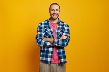 Fototapeta premium Cheerful young man keeping arms crossed while standing against yellow background