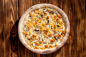 Appetizing pizza on a creamy sauce with mushrooms, corn, chicken fillet and mozzarella cheese on woden background