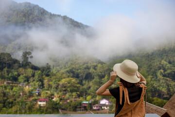 back view of woman wearing black t-shirt and hat lift smart phone up to take a photo,seeing the nature foogy over mountain,travel concept