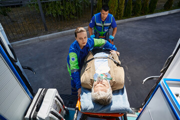 Paramedics load elderly male with breathing mask into ambulance on medical stretcher. Emergency...