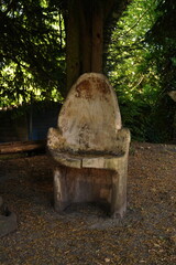 An armchair carved from wood stands in the forest under a green spruce