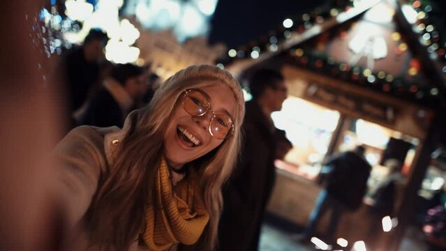 A young woman with sparklers call their relatives via video link on New Year's Eve to the chiming of the chimes in the middle of a busy street in the lights of a Christmas market on the background of