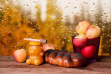 Jar with honey, braided bread and apples on windowsill with rainy autumn view