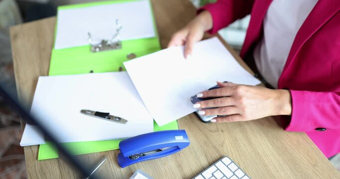 Closeup of female hands making holes with paper on documents in office