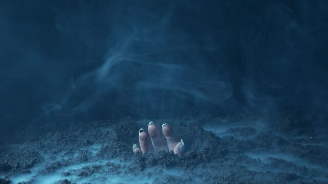 The zombie's hand breaks through the black earth in the fumes of smoke.