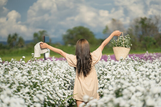A pretty girl with a hat in her hand walks into a field with field flowers.