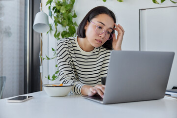 Serious female freelancer with eastern appearance keeps digital nomad lifestyle shares media and...