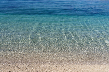 Clear water, crystal clear, seawater in various shades of blue with fine gravel as substrate. Beautiful structure and light effects from the sun shining in. Copy space for your design or product.