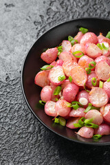 Roasted radish with spring onion and herbs in a black bowl