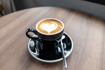 Blur,Latte coffee with heart shaped art in black cup on a wood patterned background. Close up,cup of latte coffee with a wood patterned table background. Beautyful latte art.