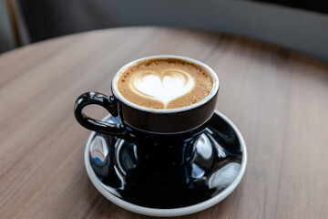 Blur,Latte coffee with heart shaped art in black cup on a wood patterned background. Close up,cup of latte coffee with a wood patterned table background. Beautyful latte art.