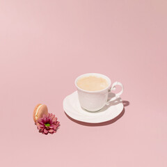 Caffe latte in a vintage style porcelain cup, macaron and flower, creative arrangement against pastel pink background. 
