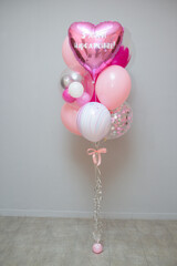 A set of pink balloons on the background of the wall, decor from helium balloons, the inscription on the pink foil balloon heart "Happy Birthday"