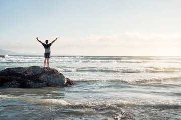 silhouette of a person on a rock on the shore of the beach with open arms looking at the horizon