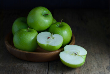 Green apples, whole, and halves are placed in a wooden tray and rest on a rustic wooden floor.