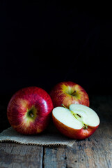 Red apples, whole, and halves put on sackcloth on a rustic wooden floor.