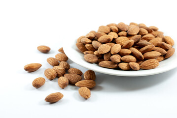 Almonds in white plate on white background with copy space, selective focus.