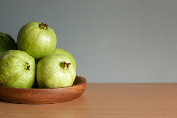 Fresh guava fruit in a wooden tray on a wooden table and grey background, space for text.