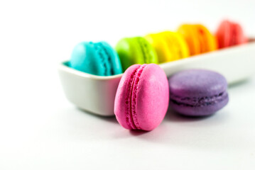 Multicolored macarons isolated on a white floor and housed in white ceramic vessels, selective focus.