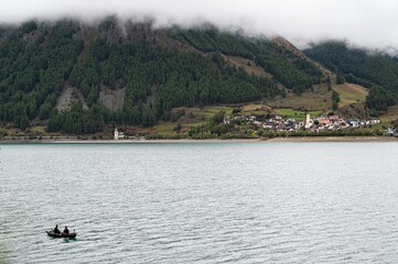 Landschaft mit zwei Anglern am Reschenstausee mit dem Ort Graun im Hintergrund