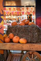 middle ages autumn harvest concept. Bunch of orange pumpkins on wood wagon with wheels,bale of hay, wooden box, backdrop bokeh blurred light bulbs and red flags. thanksgiving day, helloween