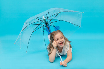 A happy cute little girl in blue rubber boots and a cotton white dress holding an umbrella lying on...