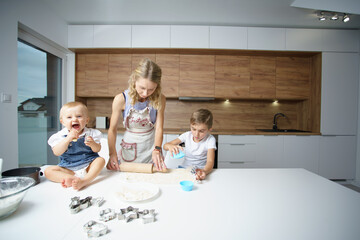 Mutter und Kinder mit Baby und Teenager spielen auf dem weißen Tisch mit Mehl in weiße Küche mit...
