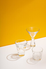 Photo of a modern stylish cocktail, alcohol glasses shot in trendy minimalistic style on a white table with yellow background
