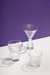 Photo of a modern stylish cocktail, alcohol glasses shot in trendy minimalistic style on a white table with purple background
