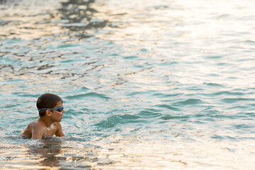 The boy in swimming goggles while standing in the seething sea. Vacation activity concept. Copy space.